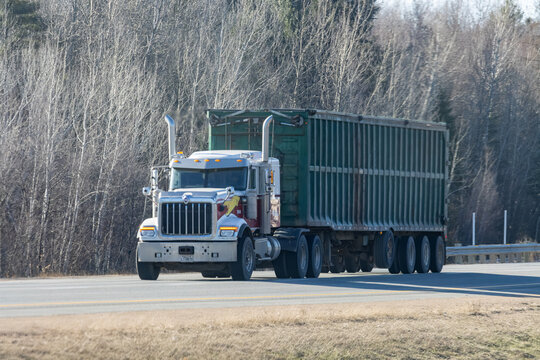 Quebec, Canada, 24 April 2026 : An International semi-truck with a green trailer drives on a highway past bare trees.