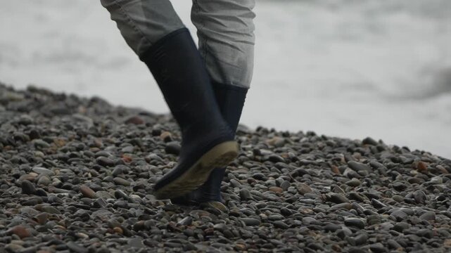 Boots walking pebbles traversing rocky beach slope near the stormy sea.