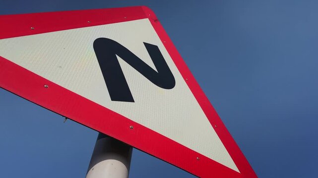 Close up view of a triangular road warning sign indicating a sharp curve ahead, set against a clear blue sky, emphasizing road safety, navigation, and transportation infrastructure.