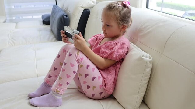 Young girl sitting comfortably with a smartphone in a bright home environment. Childhood, technology, communication and leisure concept.