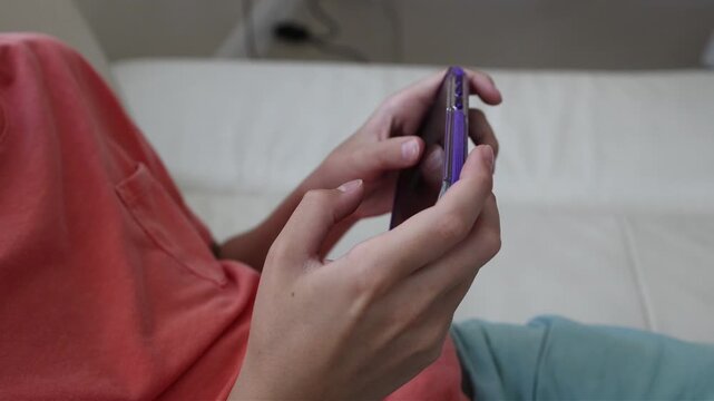 Side view of a young child using a smartphone while relaxing on a sofa indoors. Technology, communication, digital entertainment and modern family lifestyle concept.