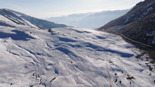 Rohtang Pass in Himachal Pradesh reveals an empty mountain road winding through snow-covered terrain between steep valley walls. Aerial perspective captures the deserted high-altitude landscape.