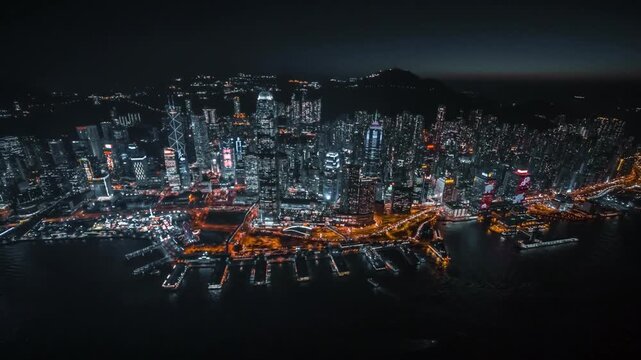 A breathtaking super wide aerial shot of Hong Kong Harbour at night, showcasing the city's iconic skyline illuminated by thousands of lights. Towering skyscrapers reflect across the water as vibrant u