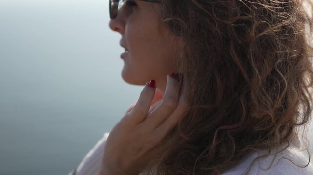 Woman, curly hair, manicure shows off her beautiful red nails while enjoying the sunny outdoor environment.