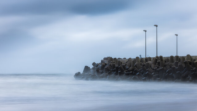 View of concrete tetrapods forming a breakwater on a misty beach with long exposure waves and street lamps Debki, Pomeranian Voivodeship, Poland.