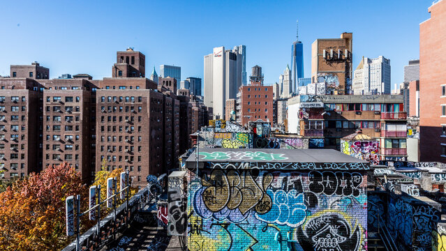 Graffiti-covered rooftops overlook the dense urban skyline of buildings and skyscrapers in Chinatown, reflecting a spirit of exploration and tourism in Lower Manhattan, New York City.