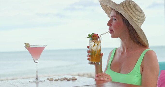 Young woman drinking passion fruit Passiflora edulis cocktail through straw, luxury beach resort overlooking ocean, tropical summer vacation setting, travel leisure lifestyle