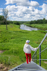 Woman walking down stairs to river, scenic summer landscape with clouds and greenery © Elena