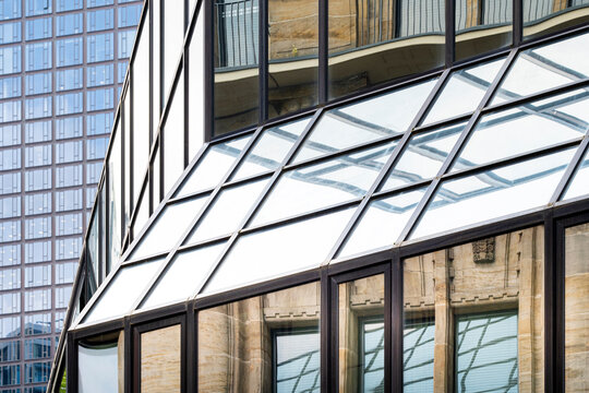 Angled urban architecture detail shows a glass facade crossing brick building windows, where geometric grid lines and blue reflection meet exterior structure