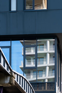A narrow urban architecture view frames a glass facade and office railing beside a stair detail, with blue reflection across window panels and vertical building lines