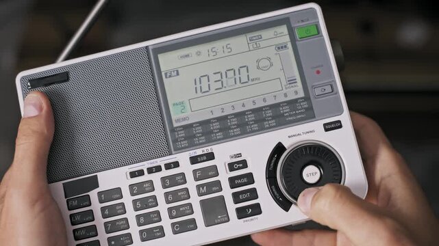 Male hands hold a portable radio receiver and turn the tuning knob to change the FM frequency on the LCD display. Concept of searching for news or entertainment signals.