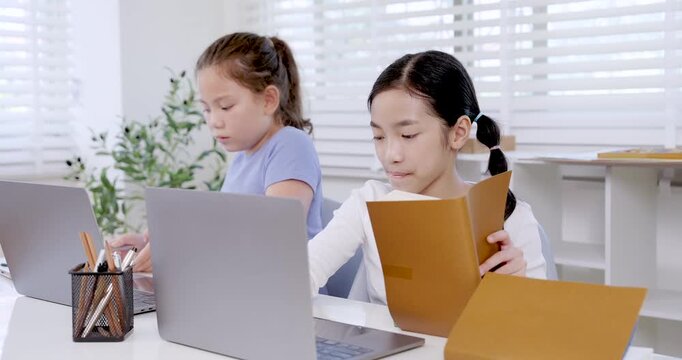Caucasian preteen girl using clipboard while asian girl holding folder beside laptop in classroom illustrating teamwork collaboration education digital learning project childhood communication