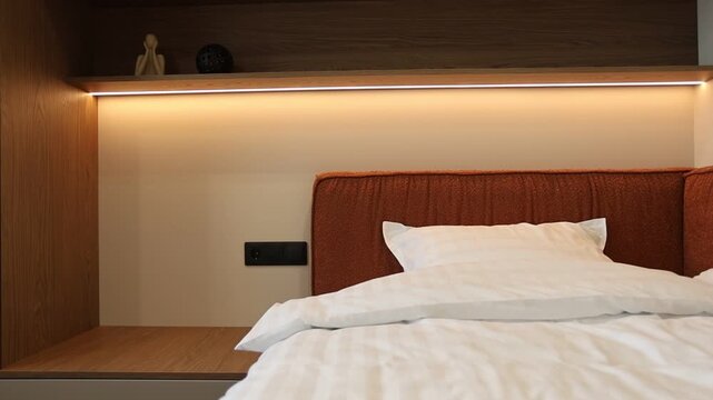 Modern bedroom alcove with made bed and warm shelf lighting