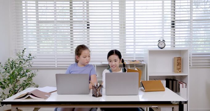 Two preteen girls asian and caucasian studying with laptops and documents in classroom representing teamwork digital learning education collaboration childhood communication research project