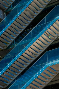 Blue metal stairs rise through urban architecture beside glass facade details, where geometric lines, structure, reflection and exterior access create depth