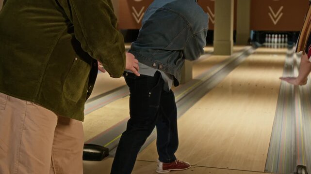 Medium rear shot of diverse friends stealing ball from cheerful black man aiming for strike at bowling alley, laughing. Video is perfect for recreational and diversity marketing campaigns