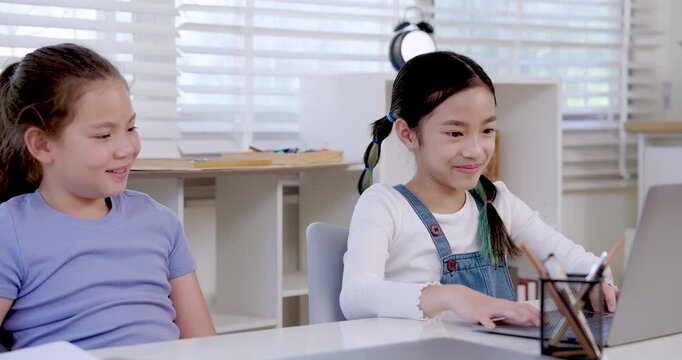 Asian girl preteen student typing laptop while caucasian girl preteen leaning forward watching together during classroom teamwork collaboration project digital learning education assignment study