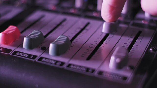 Extreme close-up of a DJ's finger pushing the MAIN fader up on a professional soundboard. Volume is adjusted near visible decibel markers under shifting purple, pink, and orange lighting.