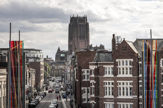 View of the Liverpool Cathedral rising above historic brick architecture and a busy city street with colorful art installations Liverpool, England, United Kingdom.
