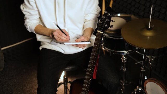 Young musician man writing lyrics for new song making notes in notebook in recording studio

