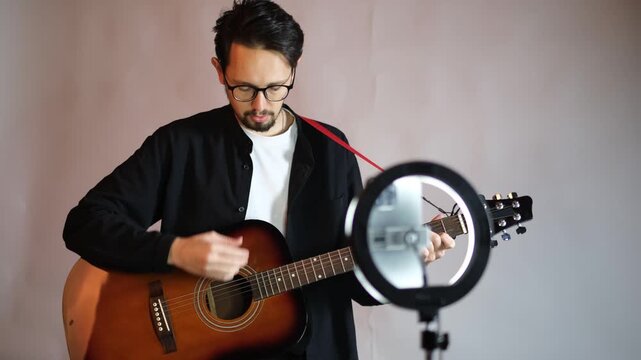 Young musician guitar teacher recording video lesson on phone with ring light in studio

