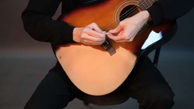 Young handsome talented guitarist in glasses replacing strings on guitar tuning it

