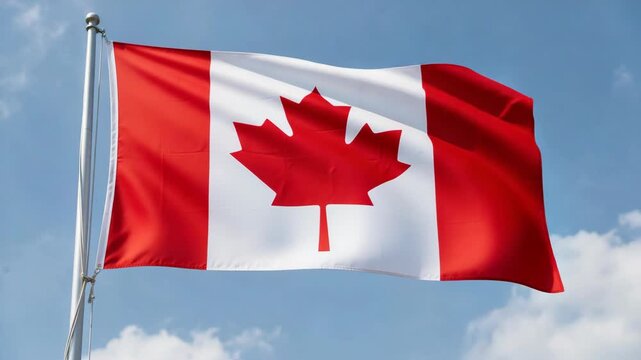 The Canadian flag flying against a clear sky with some clouds in the distance.