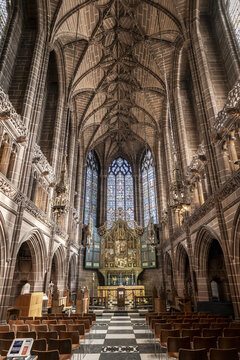 View of the ornate Gothic interior of Liverpool Cathedral featuring high vaulted ceilings, stained glass windows, and rows of wooden chairs in Liverpool, England, United Kingdom.