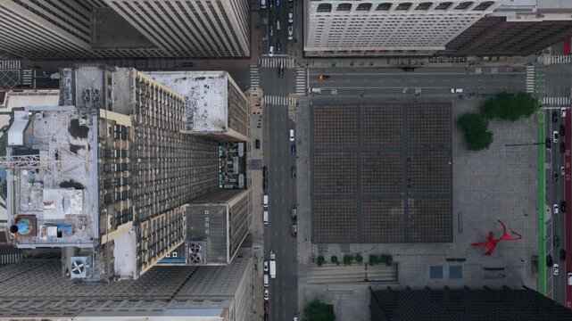 Top down flying above skyscrapers revealing Chicago Federal Plaza with Calder's Flamingo sculpture and urban traffic moving through downtown city streets