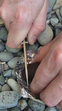 Knife chocolate slicing hands using a sharp folding knife to cut a dark chocolate candy bar on river stones outdoors for a snack