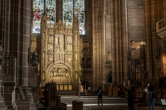 View of the ornate golden reredos and stained glass windows inside Liverpool Cathedral with visitors admiring the gothic architecture in Liverpool, England, United Kingdom.