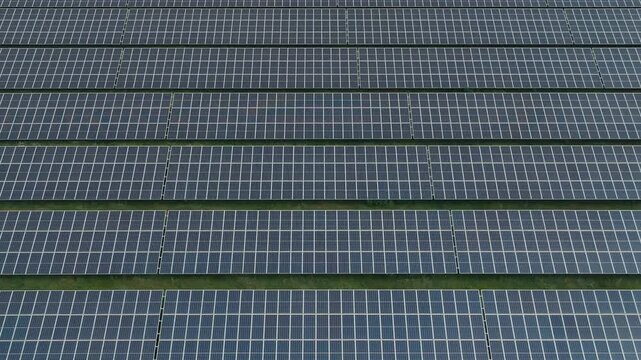 Cinematic lateral drone close-up of solar panels surrounded by lush grass. Abstract aerial footage showcasing renewable energy, sustainability, clean technology, and green power generation.