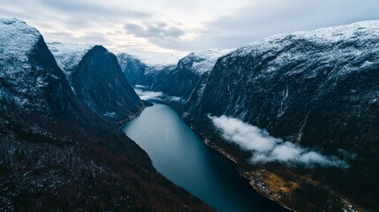 Obraz premium Winter fjord with steep, snow-capped rocky mountains and wispy clouds over calm water