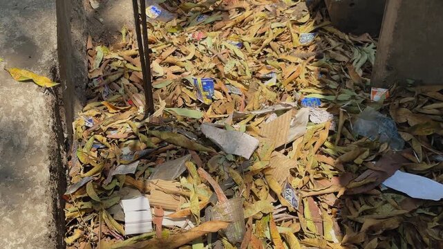 Slow tracking shot over a ground surface covered with dry fallen leaves, scattered litter, and discarded packaging, highlighting urban cleanliness challenges and environmental neglect.