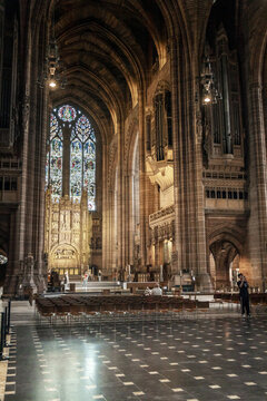 View of the grand interior of Liverpool Cathedral featuring high Gothic arches, a large stained glass window, and rows of chairs in Liverpool, England, United Kingdom.