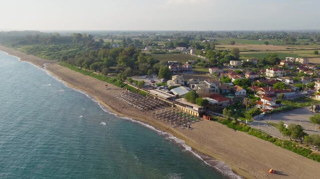 Slow panning drone shot of Kourouta beach, Greece filled with sunbeds, umbrellas and bathers during a clear summer sunny day