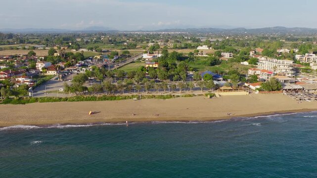 Panoramic pullback drone reveal of Kourouta beach, Greece. Beach bar umbrellas, bathers on shore. Clear sunny summer day