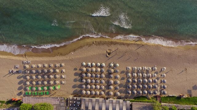 Top down drone shot of Kourouta beach, Greece. Beach umbrellas from luxury hotels and bathers visible. People swimming in clear turquoise water