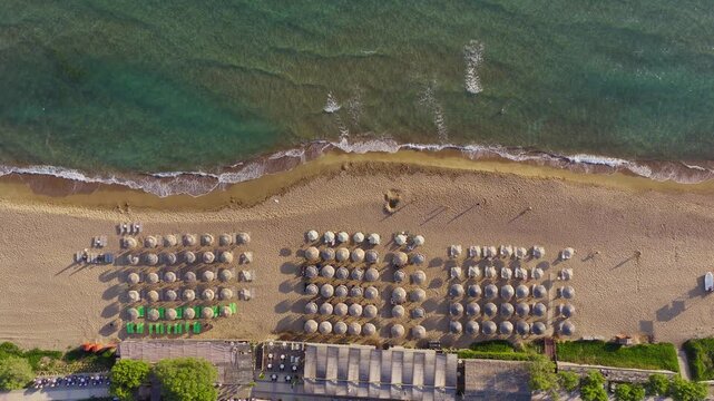 Kourouta beach, Greece. Rising top down drone shot. Luxury hotel umbrellas, bathers on shore, swimmers in sea. Clear blue water