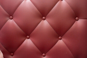 Naklejka premium Red leather upholstery with quilted pattern showing buttons in a close-up view