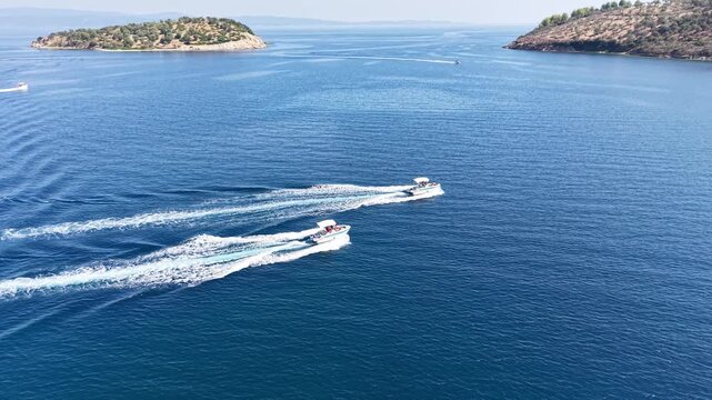 Aerial footage shows two small boats crossing blue sea and leaving parallel white wake trails behind them.