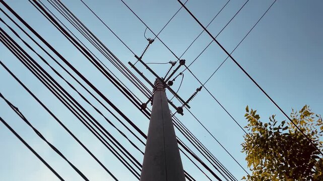 Power pole with overhead utility wires set against bright blue sky, electrical infrastructure concept featuring clean composition and outdoor industrial landscape.