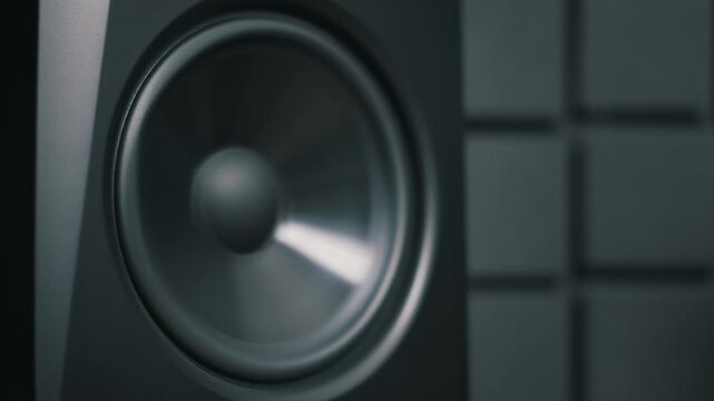 Dolly zoom out from a black speaker woofer to reveal a professional studio monitor. The high-fidelity audio equipment sits against a dark acoustic foam wall.