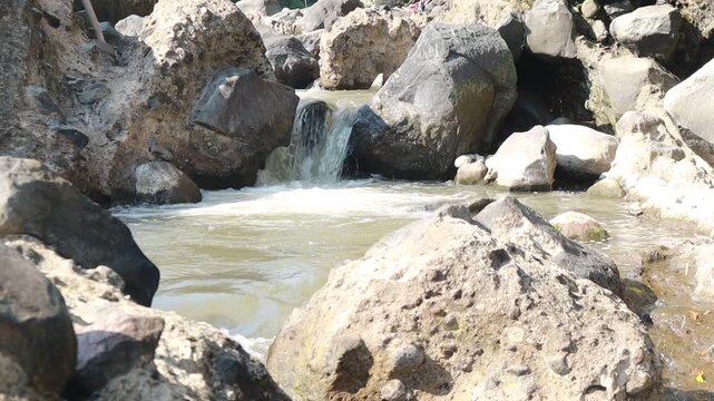 A small river stream flowing rapidly through large rocks and boulders in the countryside.