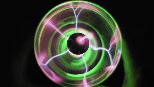 Top-down close up of a glowing plasma ball showing green and purple electric filaments moving in glass. Concept of physics experiments, scientific energy, and mysterious electric power.