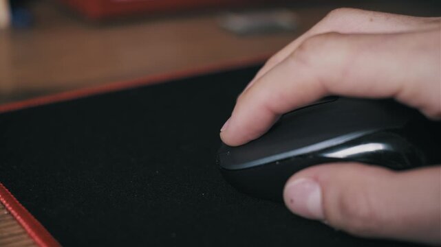 Close-up of a male hand using a black computer mouse on a mousepad with a red border. The wooden desk setting suggests a professional environment for internet browsing and corporate workflow.