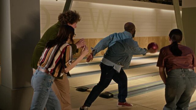 Diverse young adults cheering for African American man throwing bowling ball in alley and playing jokes. Video is perfect for marketing campaigns promoting indoor recreation and friendly gatherings