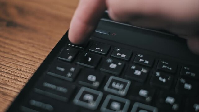 A finger repeatedly presses the Esc key on a black laptop keyboard resting on a wooden desk. This conveys concepts of frustration, troubleshooting, or attempting to exit a program.