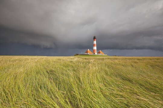Illuminated Westerheversand lighthouse on the North Sea under dark storm clouds