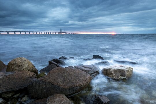 Dramatic atmosphere with sea, bridge and rocks in the foreground at sunset, &Ouml;resund Bridge, &Oslash;resundsbroen, the world's longest cable-stayed bridge, connecting Copenhagen with Malm&ouml;